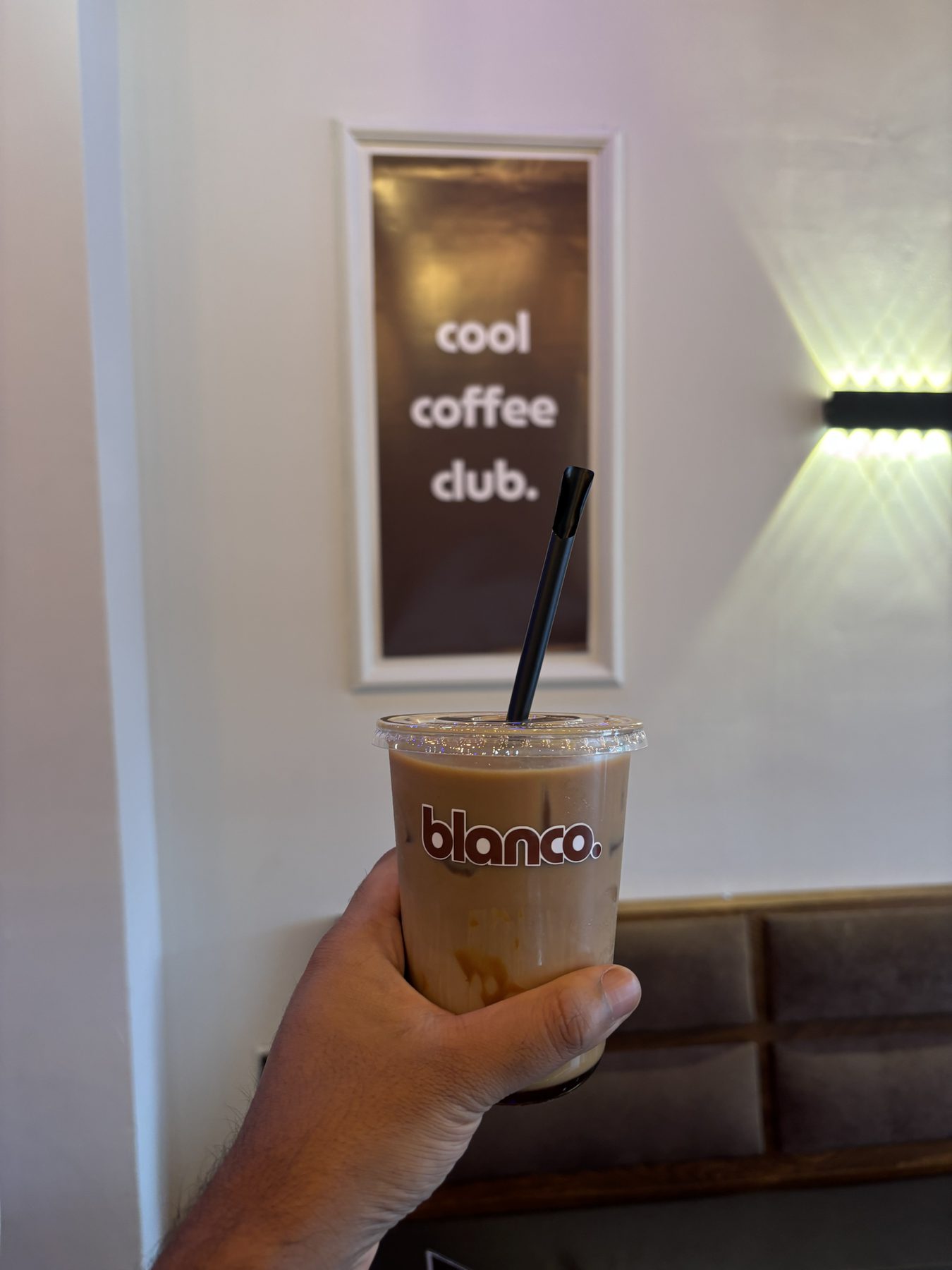 An iced Blanco latte held in front of the cool coffee club print.