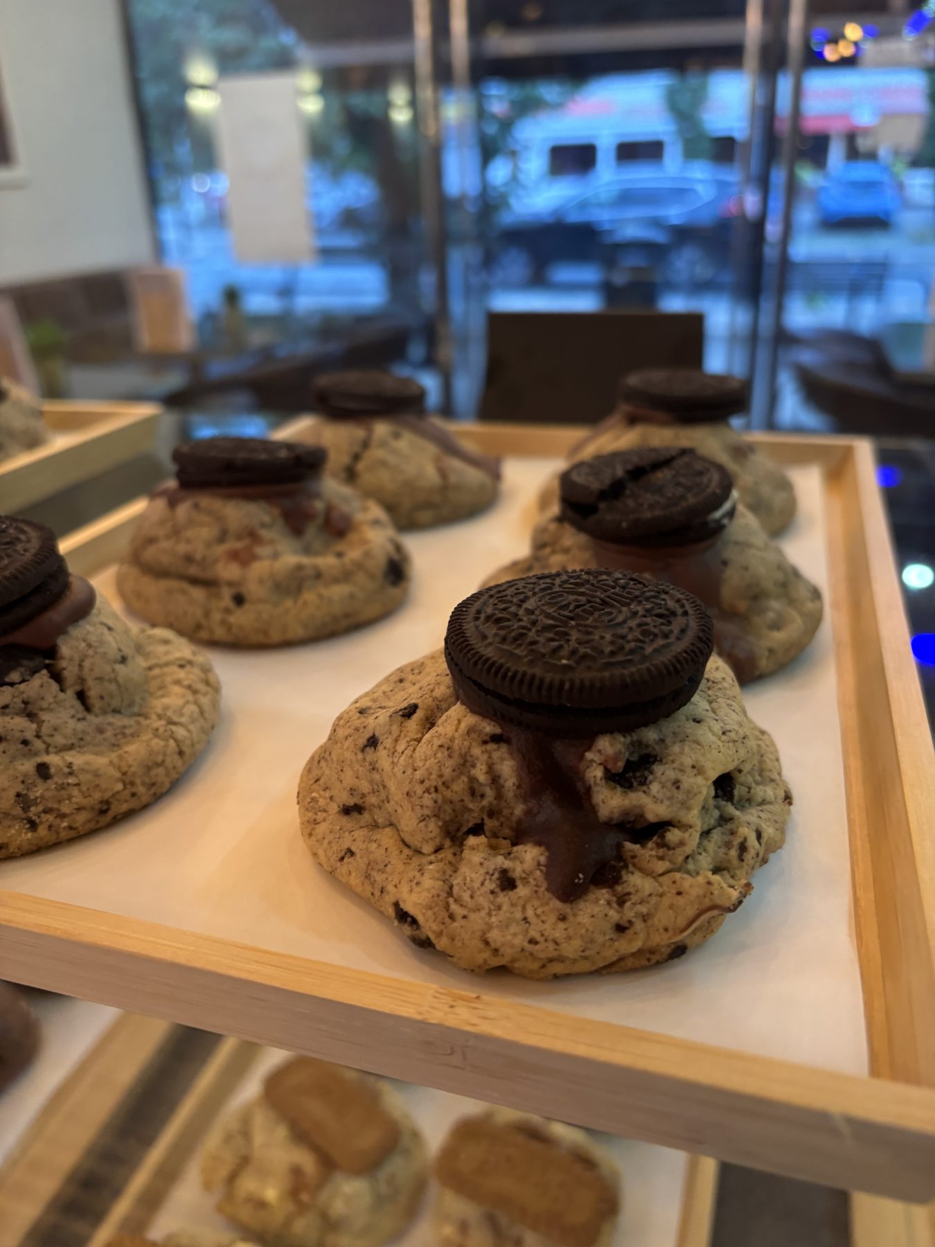 Oreo cookies on a wooden tray in the pastry case, with Biscoff cookies below and Fiveways Parade in the window.