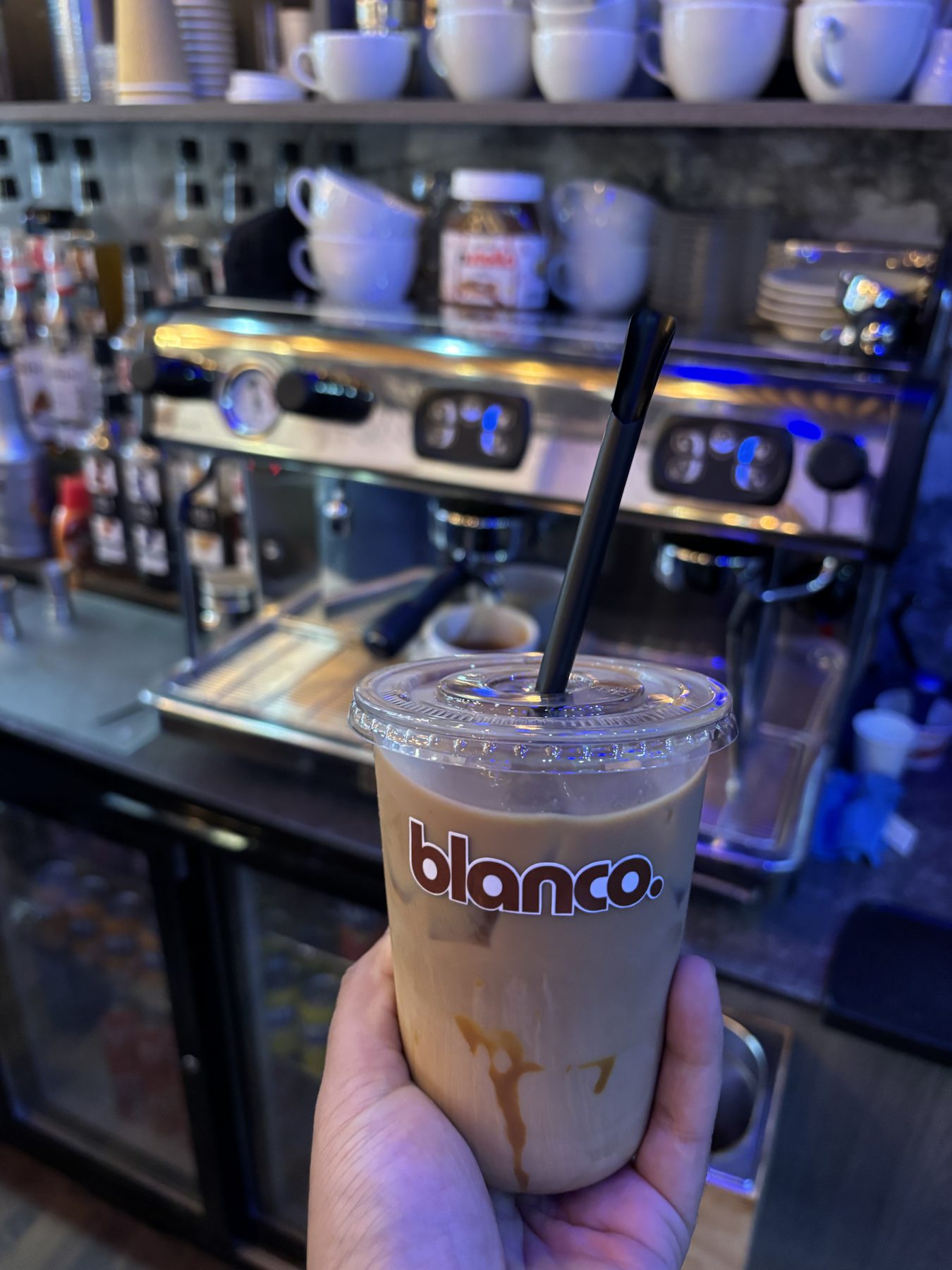 An iced Blanco latte in front of the espresso machine.