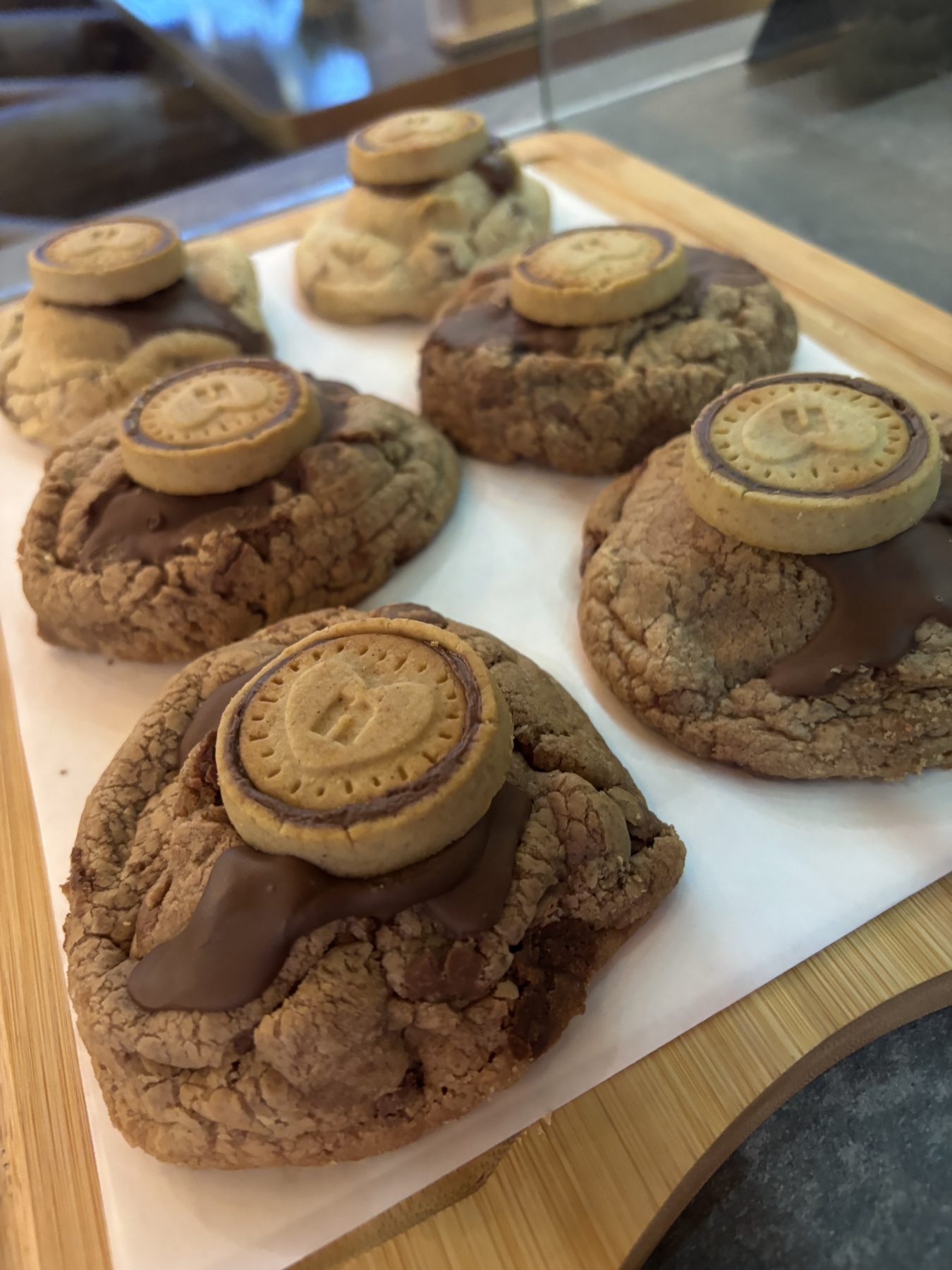 Cookies topped with melted chocolate and a heart biscuit on a wooden tray.