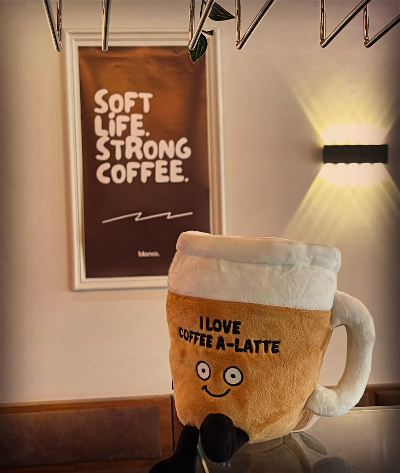 The Blanco Coffee House mug mascot in front of a Soft Life Strong Coffee print.