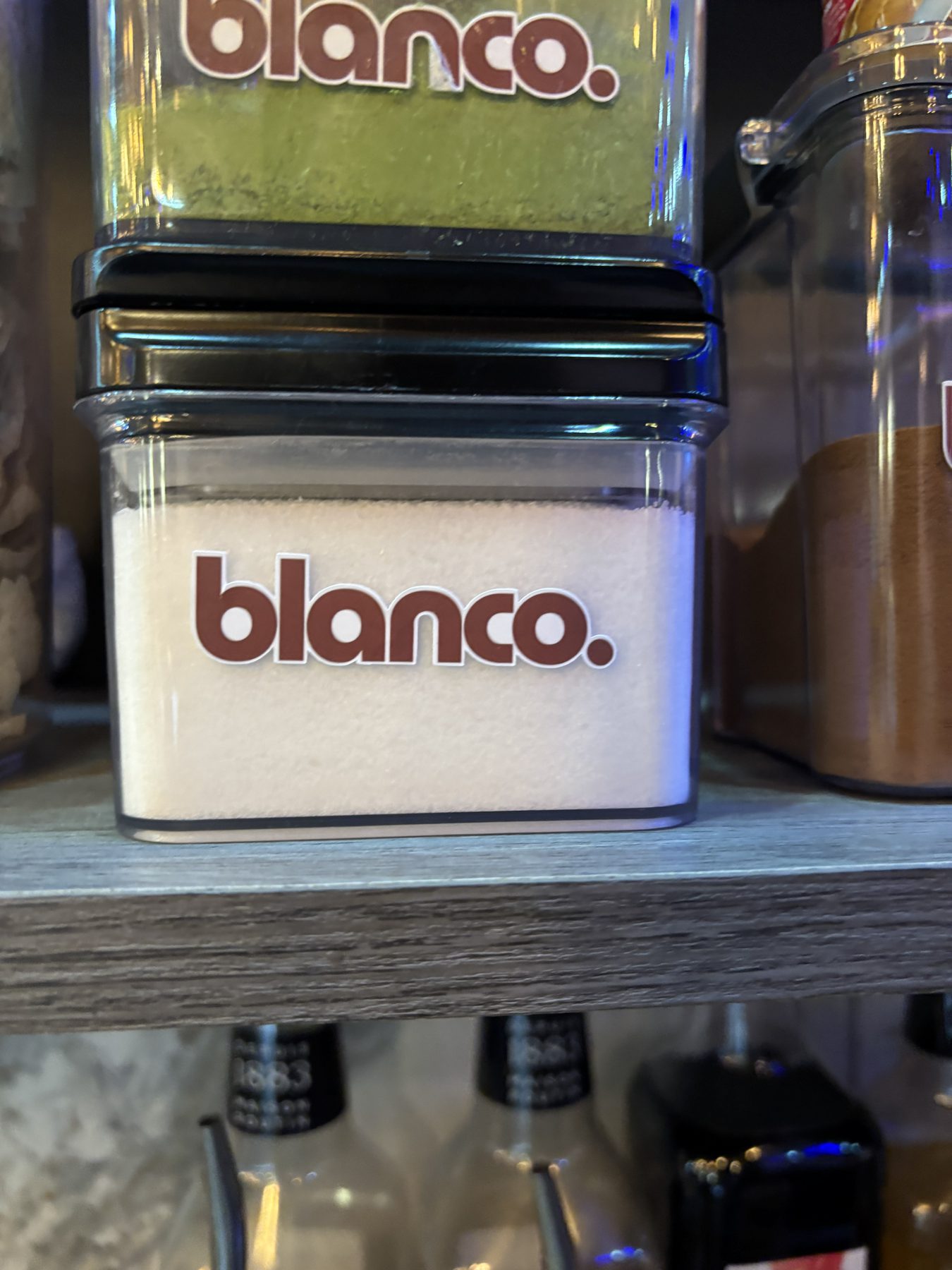 Stacked Blanco jars of sugar and matcha on the bar shelf.