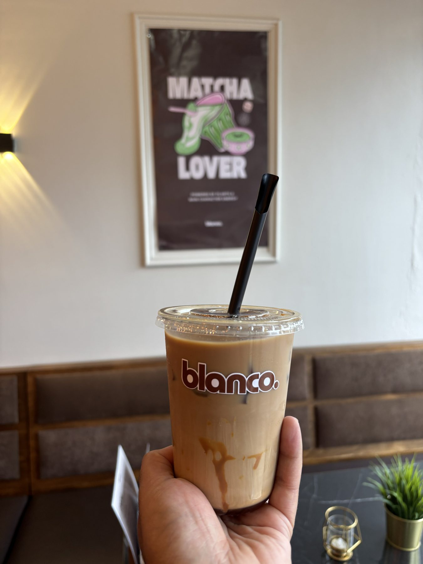 An iced Blanco latte held in front of the Matcha Lover print.