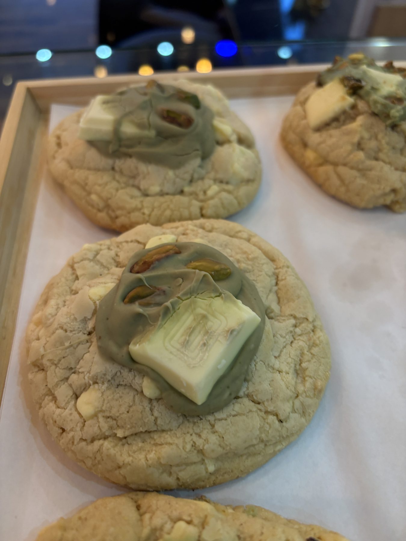 Pistachio and white chocolate cookies on a wooden tray.