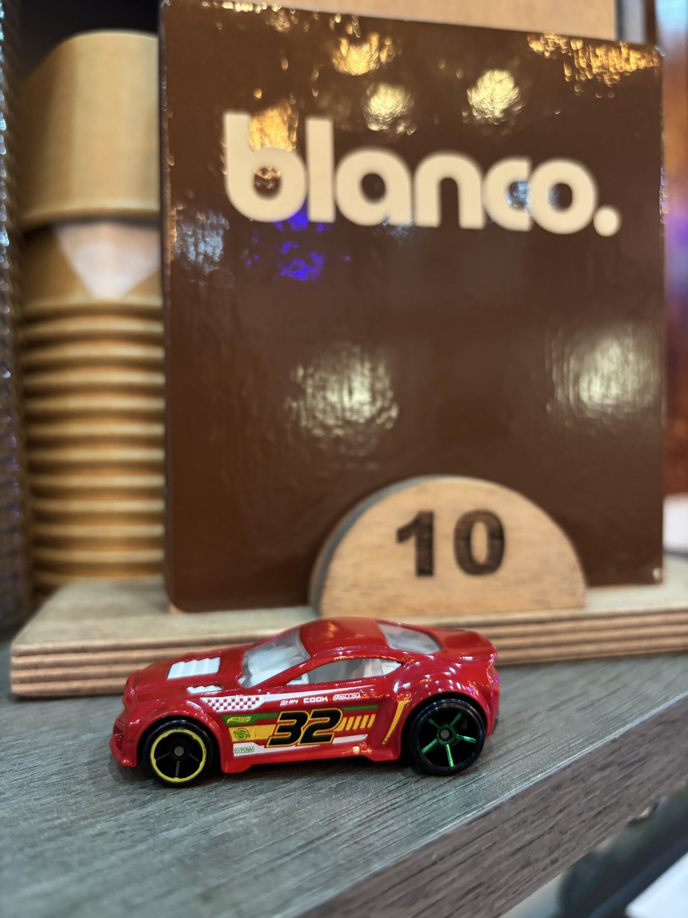 A toy car on table 10, with the blanco. sign and a stack of cups behind it.